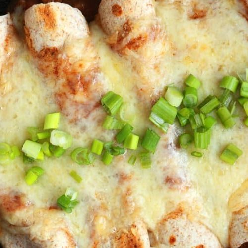 Five Mexican Enchiladas Sit In A Skillet Covered In Cheese And Green Onions.