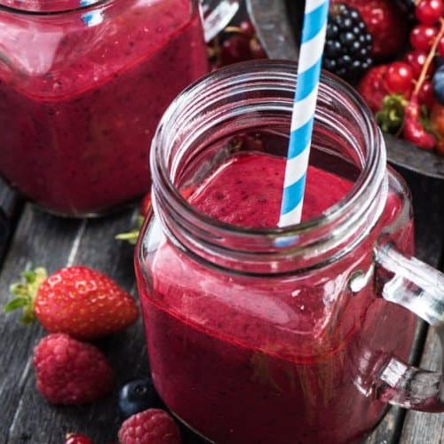 A Red Smoothie In A Cup Sits Next To A Bowl Of Assorted Berries.