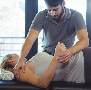 A Standing Male Chiropractic Doctor Adjusts A Female Patient Lying On Her Side.