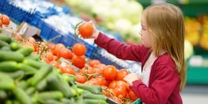 Little girl in grocery store holding a tomato making healthy eating choices