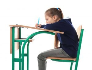 Incorrect posture concept. Little girl sitting at school desk on white background