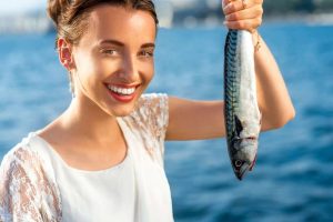 Young woman holding fresh fish outdoors on sea background