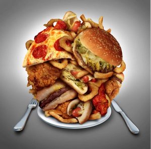 Fast food diet concept served on a plate as a mountain of greasy fried restaurant take out as onion rings burger and hot dogs with fried chicken french fries and pizza as a symbol of compulsive overeating and dieting temptation resulting in unhealthy nutrition.
