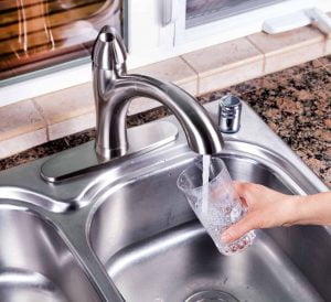 Hand holding drinking glass while being filled with tap water from kitchen faucet.