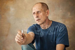 Worried mature man sitting at studio, smoking and thinking about something