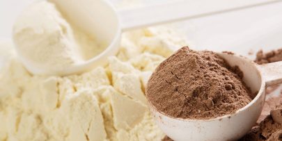 piles of chocolate and vanilla protein powders each with a white plastic scoop sitting on top